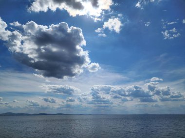 Güneş ışığındaki kümülüs bulutları mavi gökyüzünde denizin üzerinde.