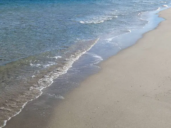 Boş kumsaldaki deniz kenarı. Deniz suyu ve kara arkaplanı çapraz olarak ikiye böler