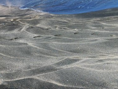 Dalgaların dantelli izleri denizin kenarındaki siyah kumda.