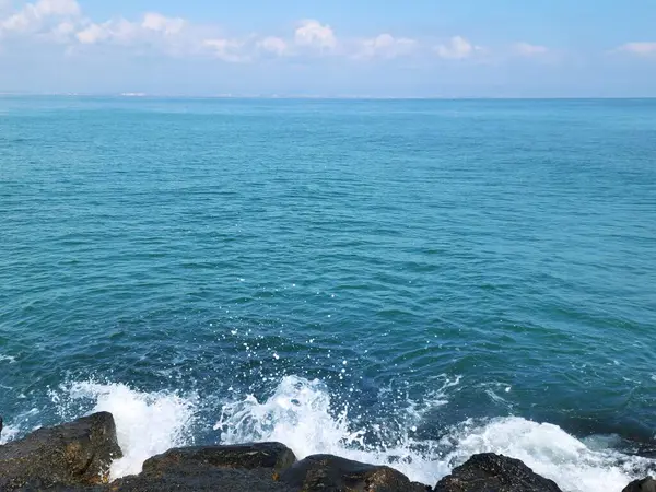 Parlak mavi deniz arka planı. Beyaz dalgalar kayalara çarpıyor.
