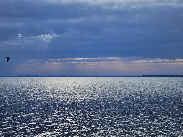 Fırtınalı mavi gökyüzü altında akşam manzarası parlayan gümüşi deniz yüzeyi