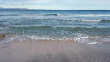 Sığ deniz, kumlu sahile yumuşak dalgalar saçar.