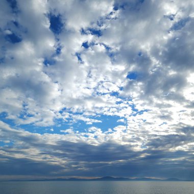 Büyük bulutlu gökyüzünün altında alçak deniz ufku. Akşam deniz manzarası ve mavi dağlar.
