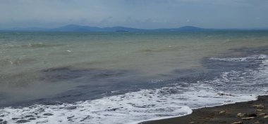 Fırtınalı denizin azgın suları siyah kumlu kıyıları hoş bir manzarada köpüklü dalgalarla doldurur.