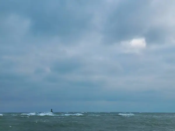 Fırtınalı denizin üzerinde akşam manzarasında yumuşak fırtınalı bir gökyüzü. Dalgaların arasında uzak deniz feneri