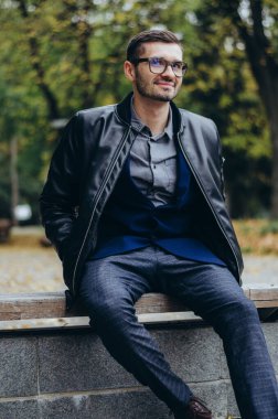 Gözlüklü genç bir adam bankta oturuyor.