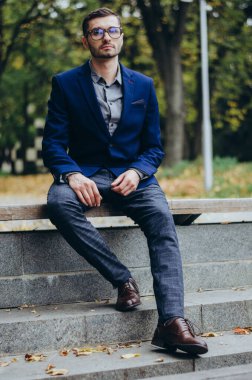 Gözlüklü genç bir adam bankta oturuyor.