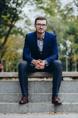 Takım elbiseli bir adam parkta bankta oturuyor.