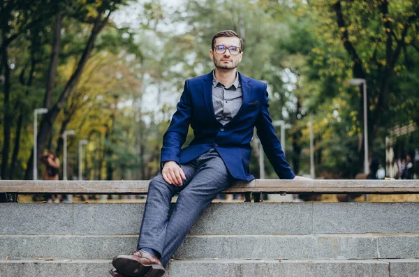 Takım elbiseli bir adam parkta bankta oturuyor.