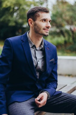 Takım elbiseli bir adam bankta oturuyor ve gülümsüyor.