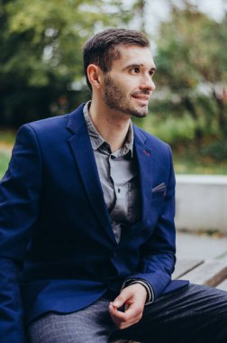 Takım elbiseli bir adam bankta oturuyor ve gülümsüyor.