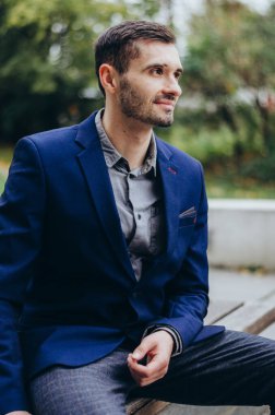 Takım elbiseli bir adam bankta oturuyor ve gülümsüyor.