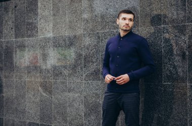 Elinde gözlük olan bir adam duvarın yanında duruyor.