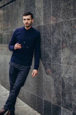 Elinde gözlük olan bir adam duvarın yanında duruyor.