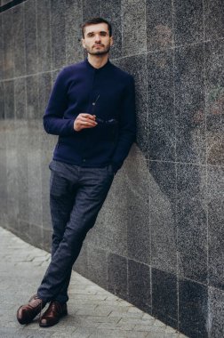 Elinde gözlük olan bir adam duvarın yanında duruyor.