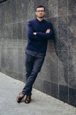 Elinde gözlük olan bir adam duvarın yanında duruyor.