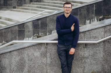 Korkulukların yanında gözlüklü genç bir adam.