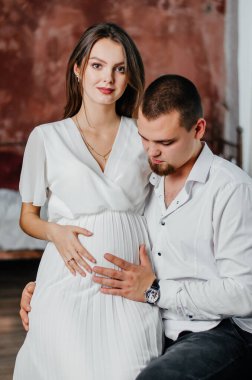 a pregnant girl sits on a man's lap