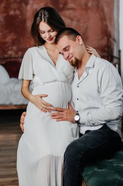 a pregnant girl sits on a man's lap