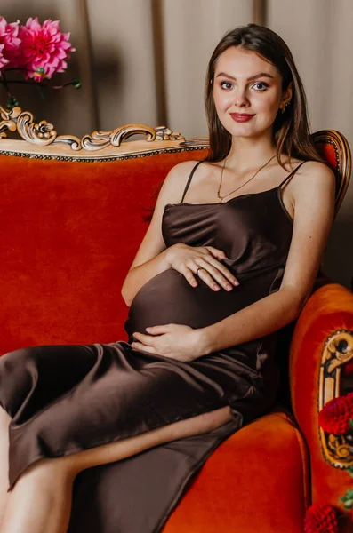 stock image A pregnant woman sits on a red couch with a bouquet of flowers in the background