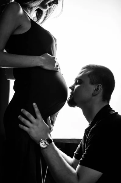 男はお腹の中で妊娠中の妻とキスをする 白黒写真 — ストック写真