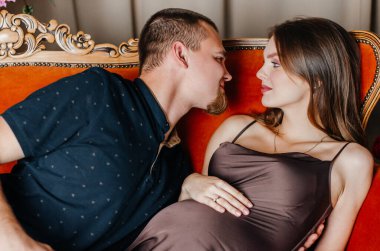 Hamile bir kadın kocasıyla kanepede yatıyor.