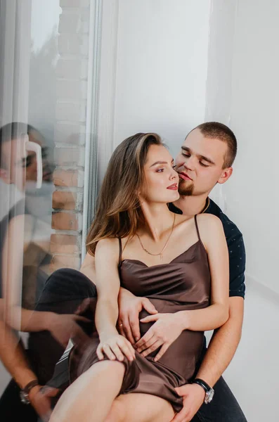 男と妊婦が窓辺に座って抱き合っている — ストック写真