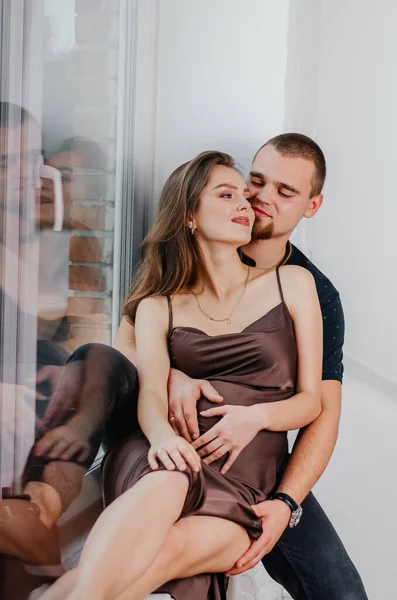 Bir Adam Hamile Bir Kadın Pencere Eşiğinde Oturmuş Birbirlerine Sarılıyorlar — Stok fotoğraf