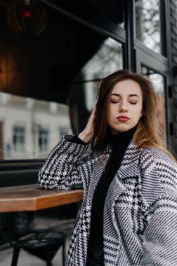 Gri bir kazak ve kot pantolon giyen bir kadın bankta oturuyor.