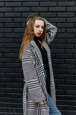 Siyah tuğlalı duvarın önünde duran ceketli bir kadın.