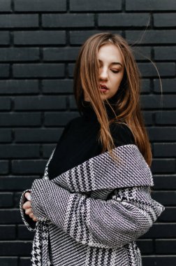 Siyah tuğlalı duvarın önünde duran ceketli bir kadın.