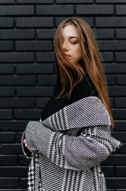 Siyah tuğlalı duvarın önünde duran ceketli bir kadın.