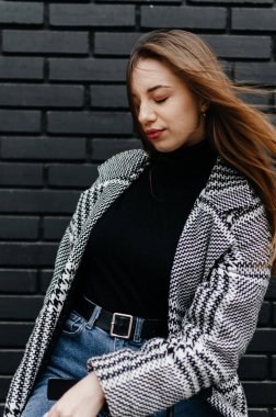 Siyah tuğlalı duvarın önünde duran ceketli bir kadın.