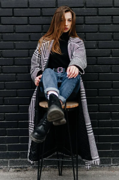 stock image a girl in a gray coat sits on a chair near a black wall