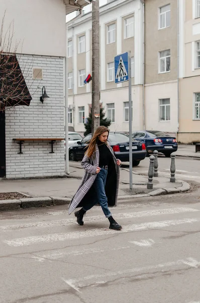 stock image A woman crossing the street in a coat and jeans