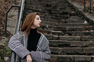 Merdivenlerin yanında ceketli bir kız var.