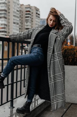 Paltolu ve kot pantolonlu bir kadın korkuluğa yaslanıyor.