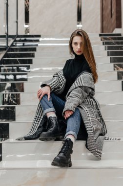 Ceketli bir kız merdivenlerde oturuyor.