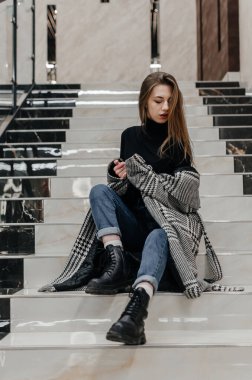 Ceketli bir kız merdivenlerde oturuyor.