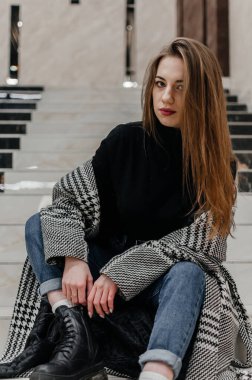 Ceketli bir kız merdivenlerde oturuyor.