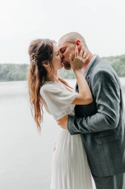 Gelin ve damat göl kıyısında sarılıp öpüşürler.