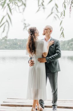 Gelin ve damat göl kıyısında sarılıp öpüşürler.