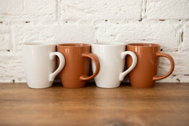 Kahverengi ve beyaz bardaklar beyaz bir duvarın yanındaki ahşap bir masada duruyor.