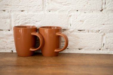 İki kahverengi bardak, beyaz bir duvarın yanındaki tahta bir masada duruyor.