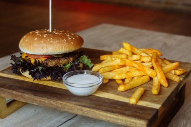 Kürdanlı bir hamburger kesme tahtasının üzerinde patates kızartması ve meze ile duruyor.