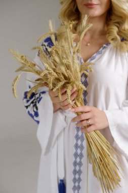 İşlemeli elbiseli bir kadın buğday kulakları tutuyor.