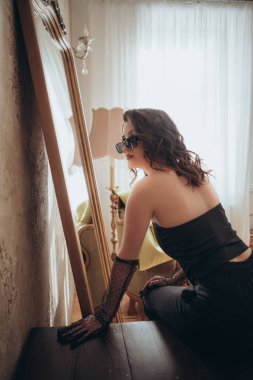Siyah korseli şık kadın aynanın karşısında zarif bir şekilde poz veriyor.