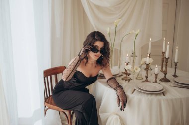 Süslü masada siyah elbiseli zarif bir kadın.