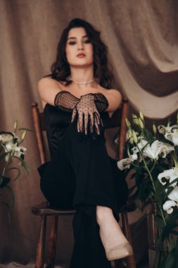 Zambakların arasında oturan yoğun bakışlı manken.