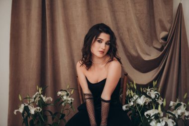 Tarafsız tonlar ve zambaklarla çerçevelenmiş siyah elbiseli düşünceli kadın.